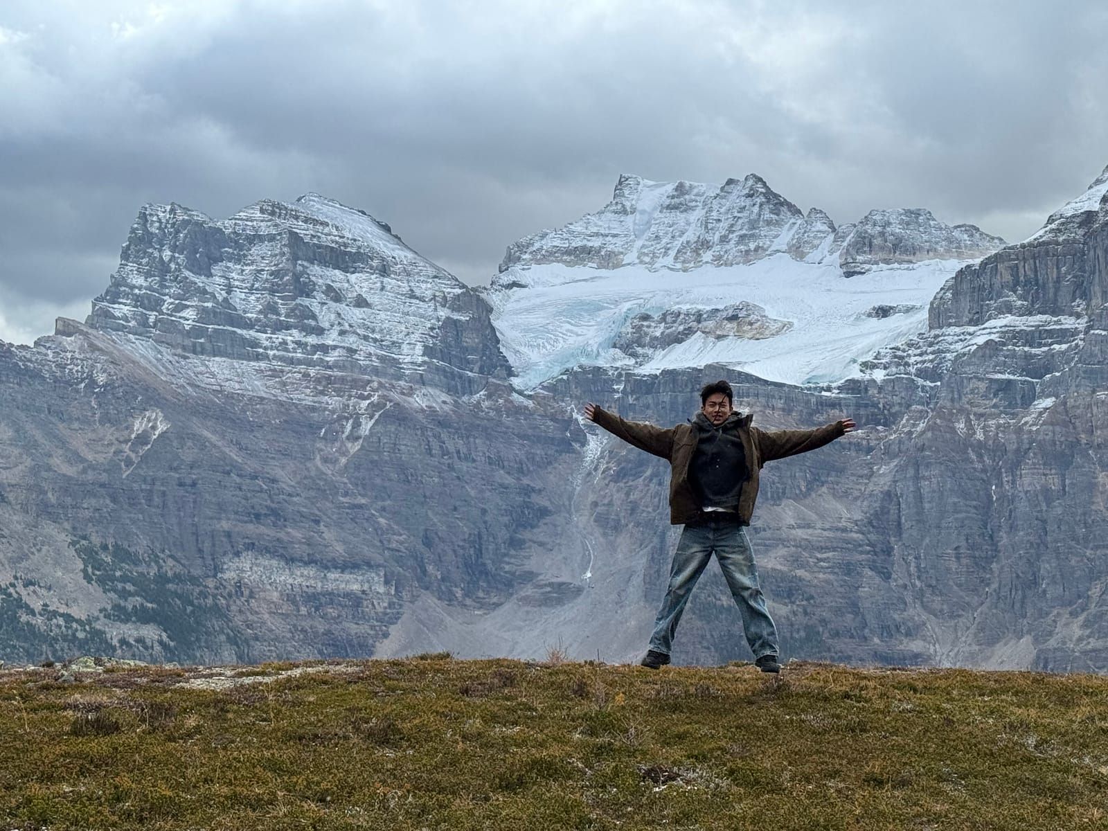 Joshua standing with arms outstretched below a glacier in the Rockies