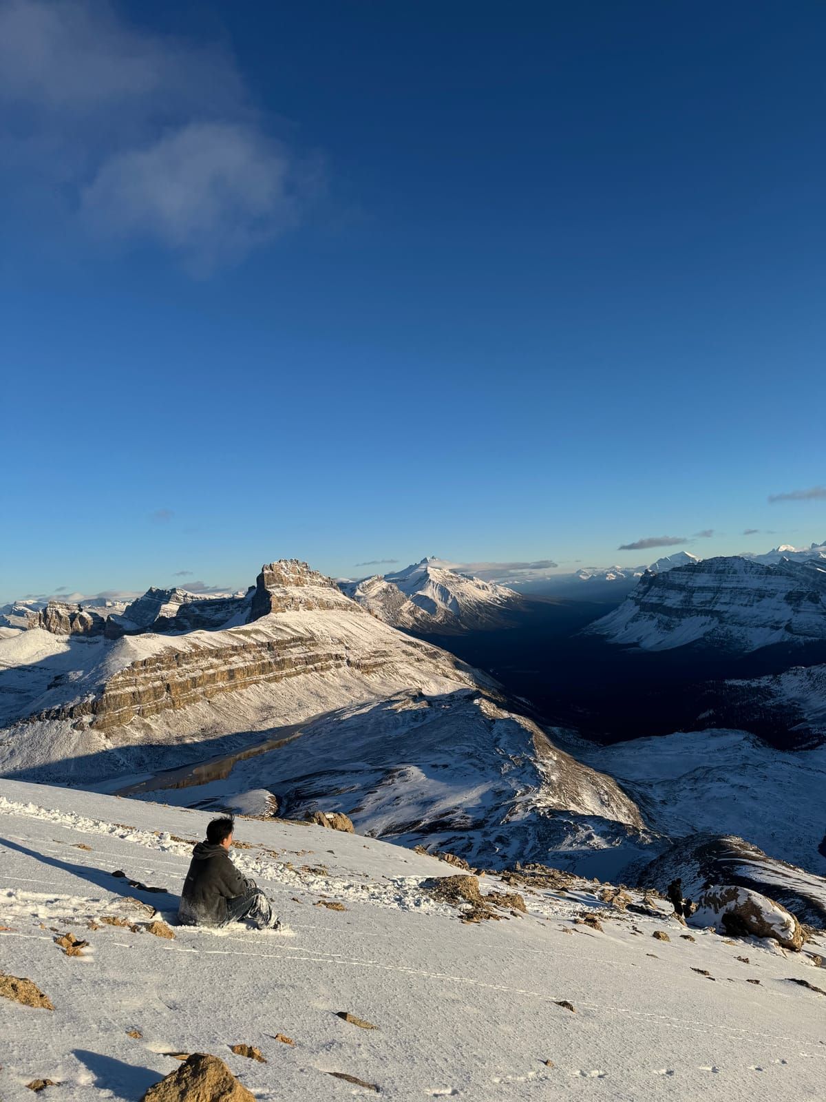 Joshua sitting on a snowy ridge looking out over the Canadian Rockies at golden hour